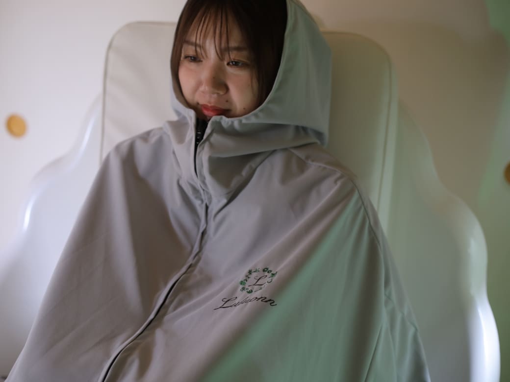 ルルオン専用ポンチョをまとい、緑のミストに包まれておだやかにくつろぐ女性